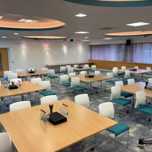 A modern conference room with multiple tables, teal and white chairs, set for a meeting with water bottles and stationery.