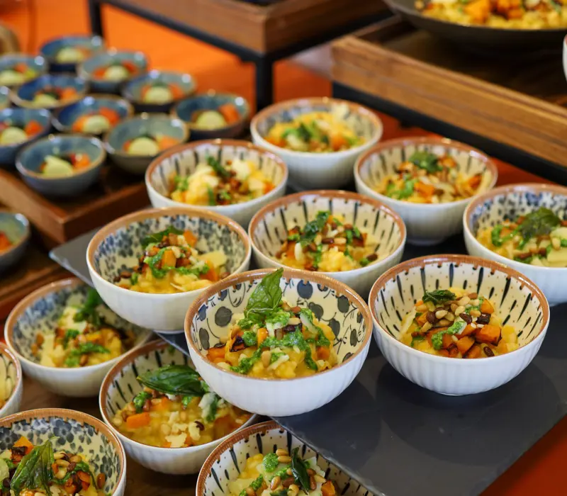 Colorful, patterned bowls filled with a mixed salad of vegetables and greens, arranged on a buffet table.