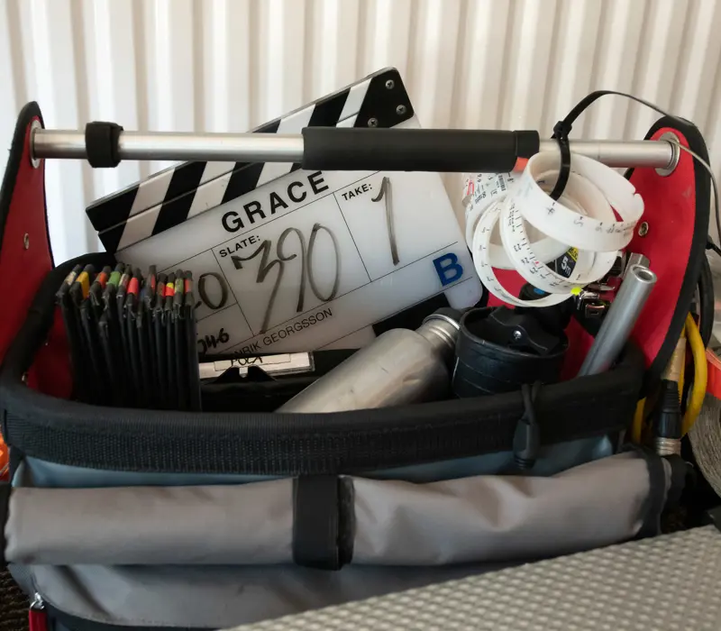Film set equipment bag with a clapperboard labeled "Grace," pencils, tape rolls, and metal water bottles.