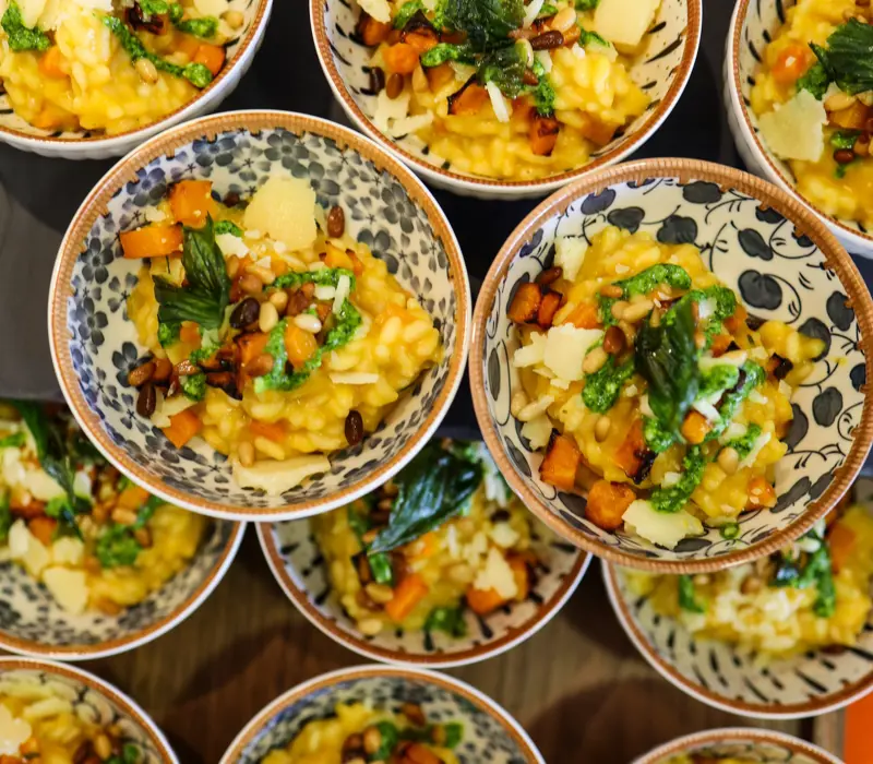 Bowls of risotto with asparagus, pine nuts, and cheese garnished with herbs, arranged neatly on a table.