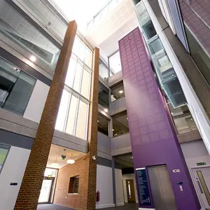 Modern building atrium with tall brick and purple columns, glass windows, and multiple floors, viewed from below.