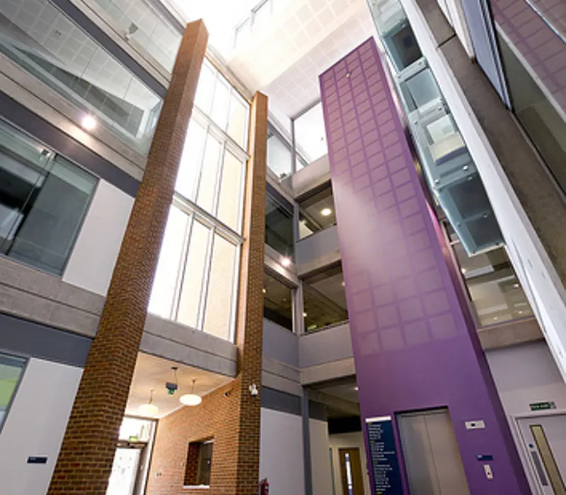 Modern building atrium with tall brick and purple columns, glass windows, and multiple floors, viewed from below.