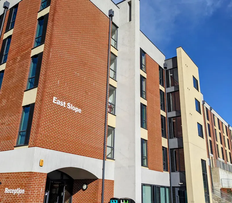 Four-story red brick and beige building labeled East Slope with a clear blue sky background.