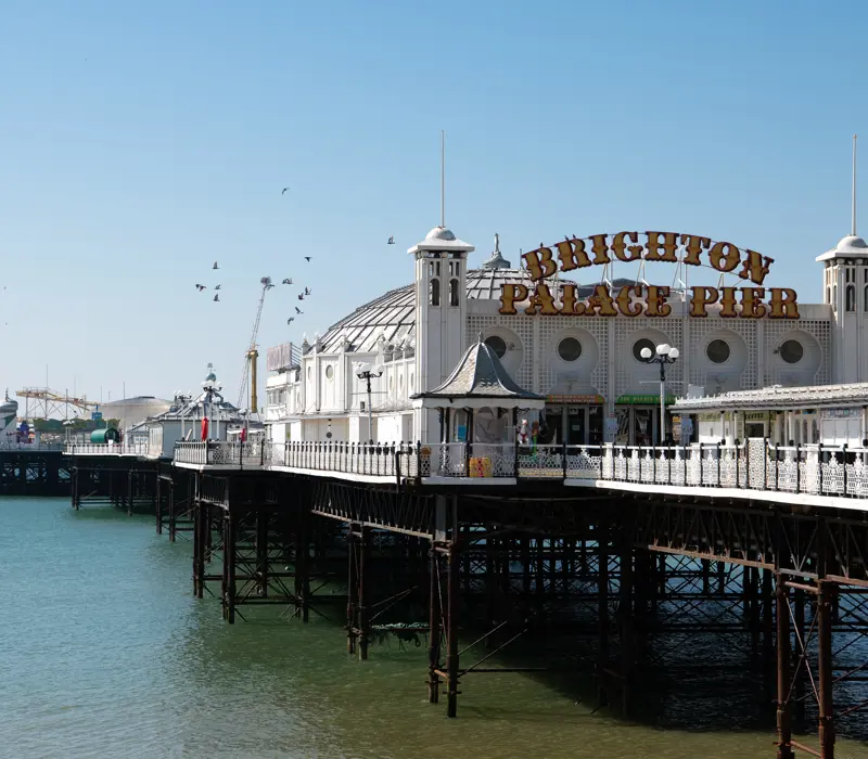 Brighton Palace Pier extends over the sea under a clear blue sky, with seagulls flying above.