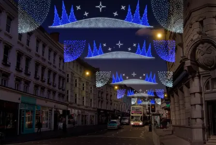 City street at night with festive blue and white light decorations, featuring tree shapes and stars, above the road.