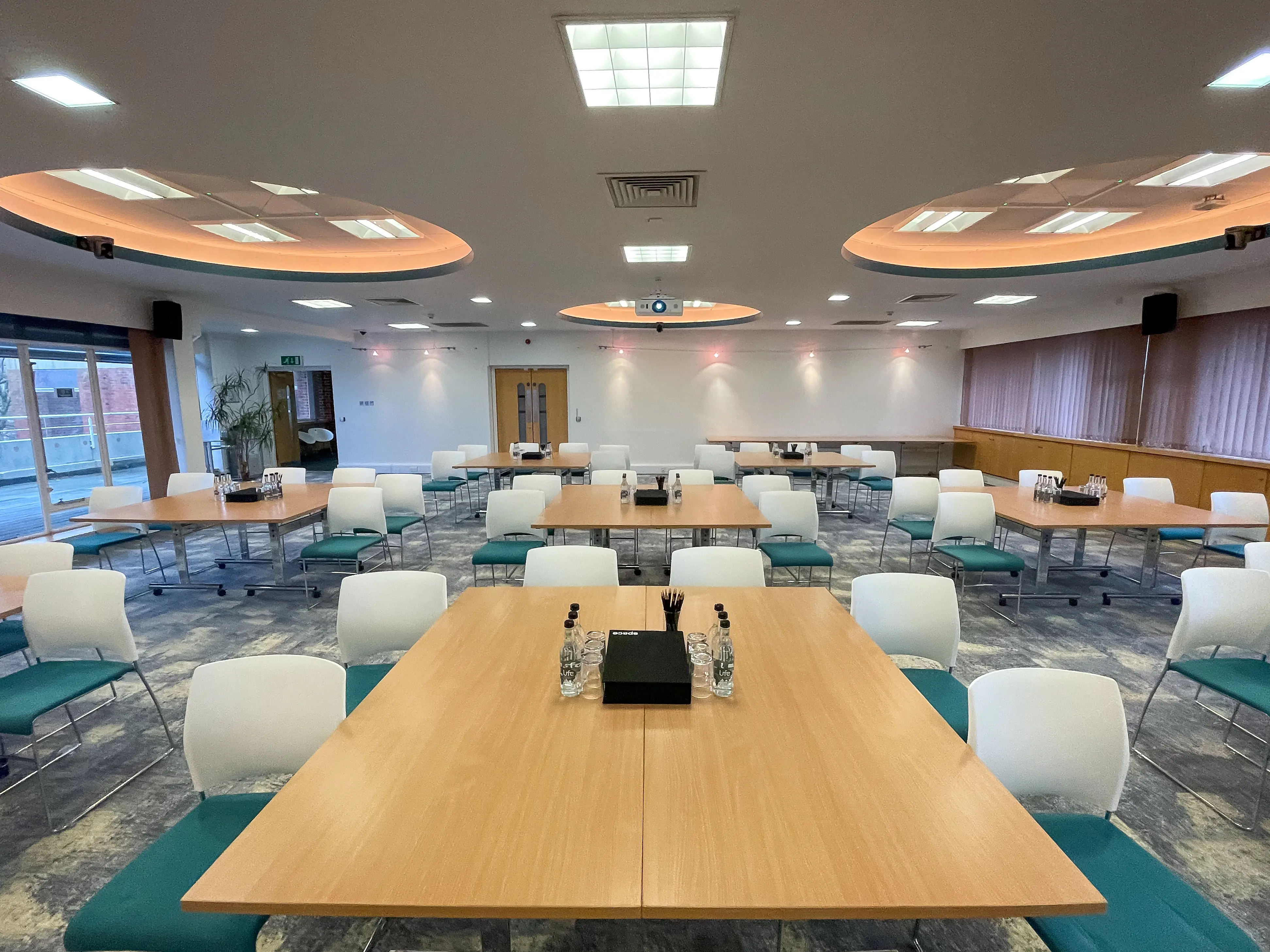 Spacious conference room with arranged tables, chairs, water bottles, and ceiling lights, ready for a meeting.