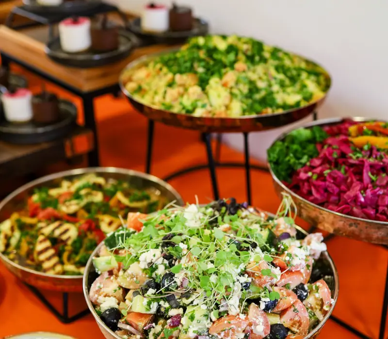 A variety of colorful salads in bowls, including mixed greens, couscous, and vibrant vegetable mixes on an orange table.