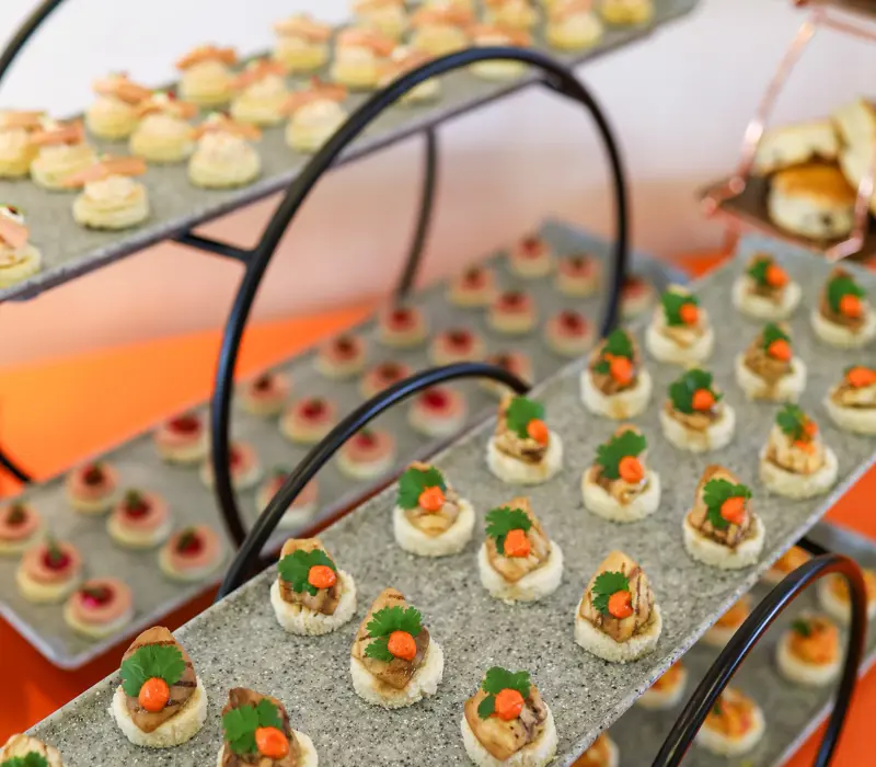 Tiered trays display assorted canapés with vibrant toppings, set on a granite surface.
